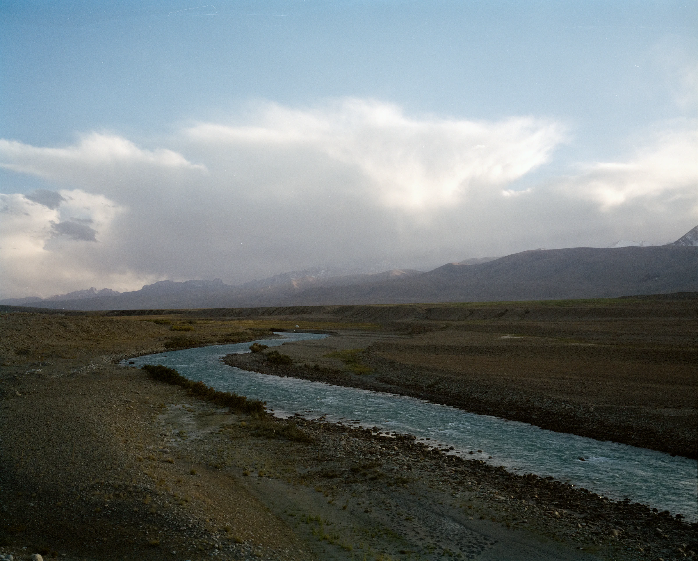 弯曲河道穿过开阔草地，低云压在远山上方