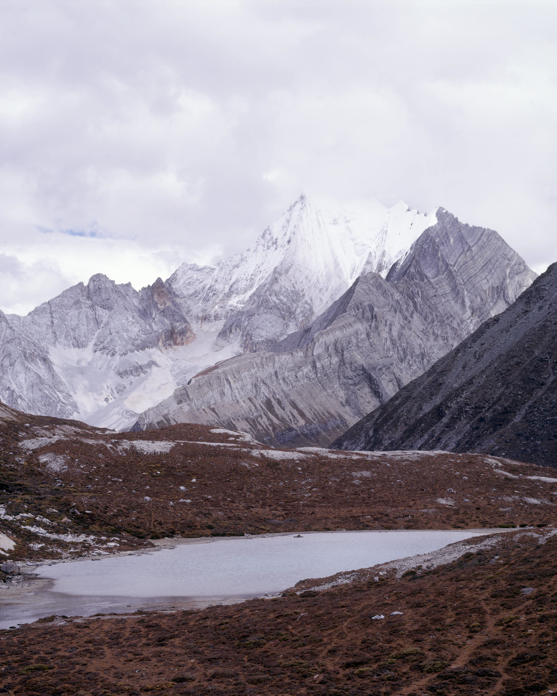 积雪群峰环绕一片高山湖泊，前景是深色荒地