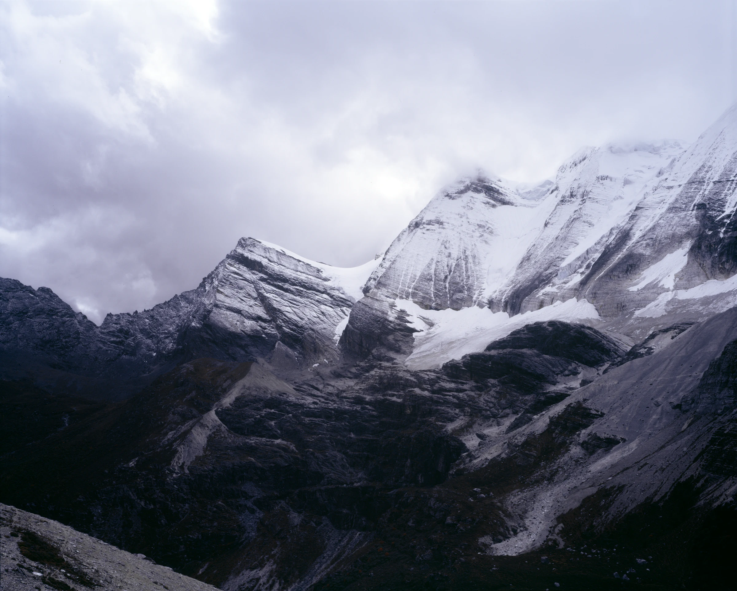 积雪山峰从云雾中显露，深色山谷延伸至前景
