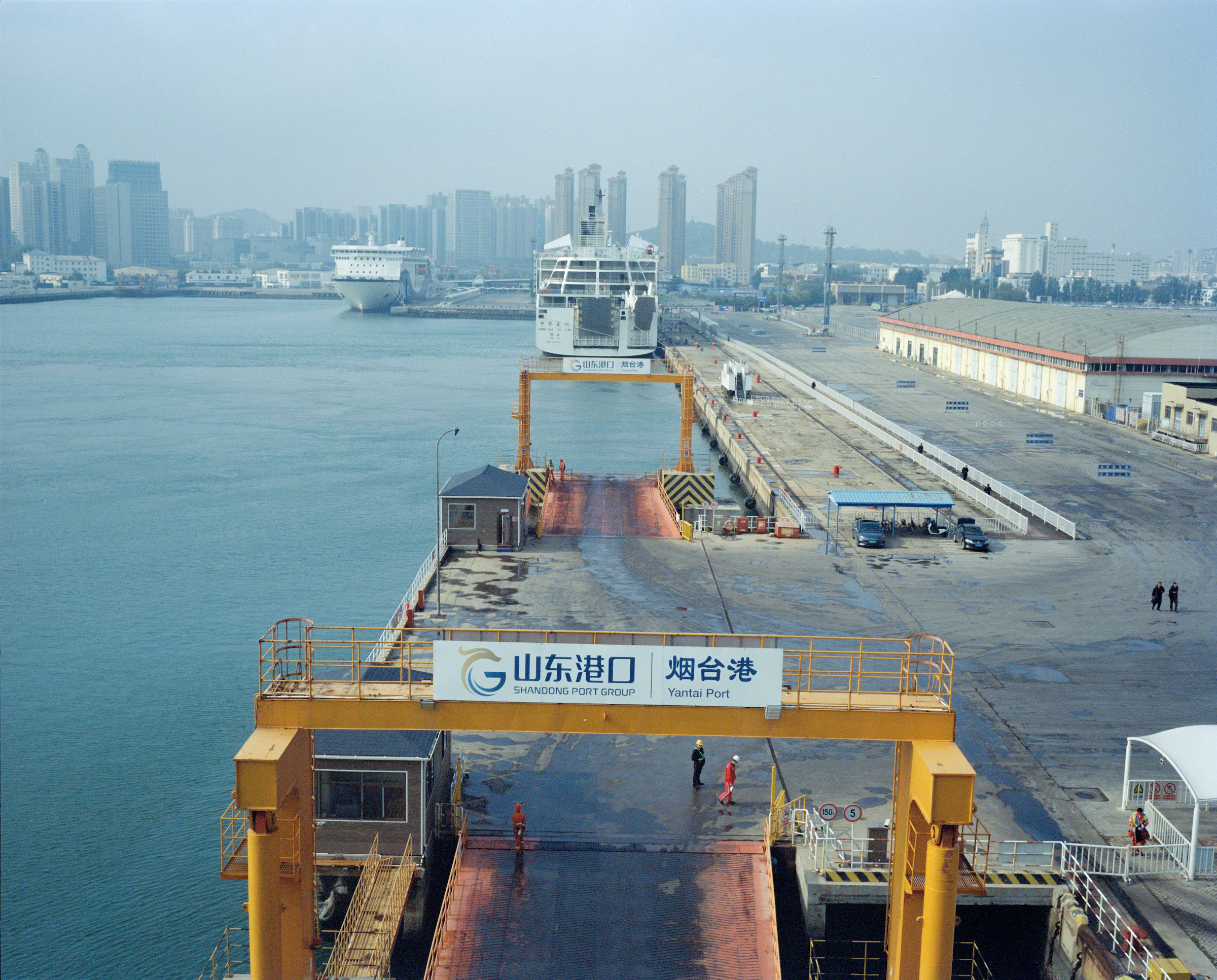 带有“山东港口 烟台港”字样的黄色港口设施、船只与远处城市临水展开
