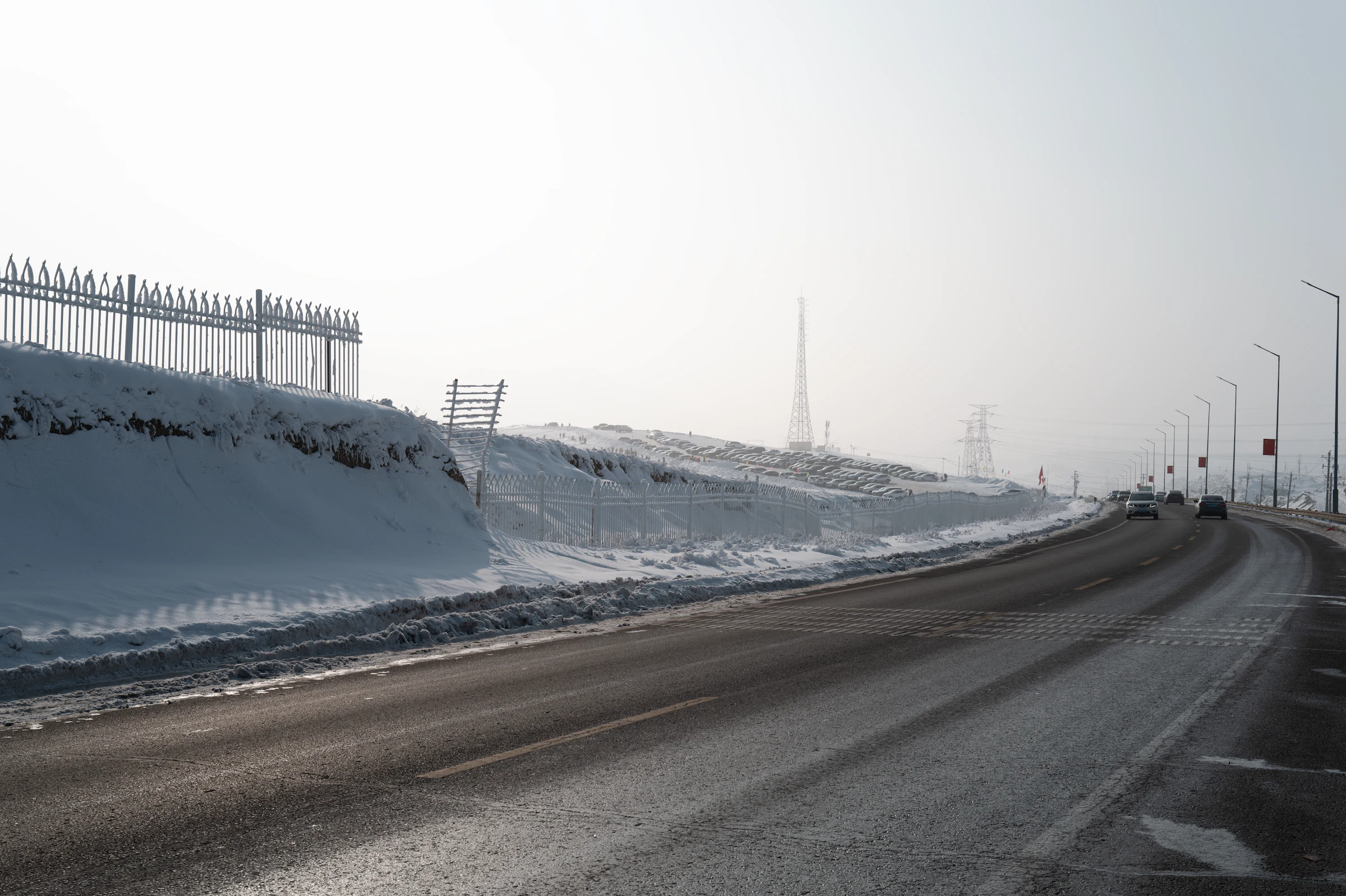 新疆乌鲁木齐一条公路穿过积雪旷野，电线杆延伸至雾色远方